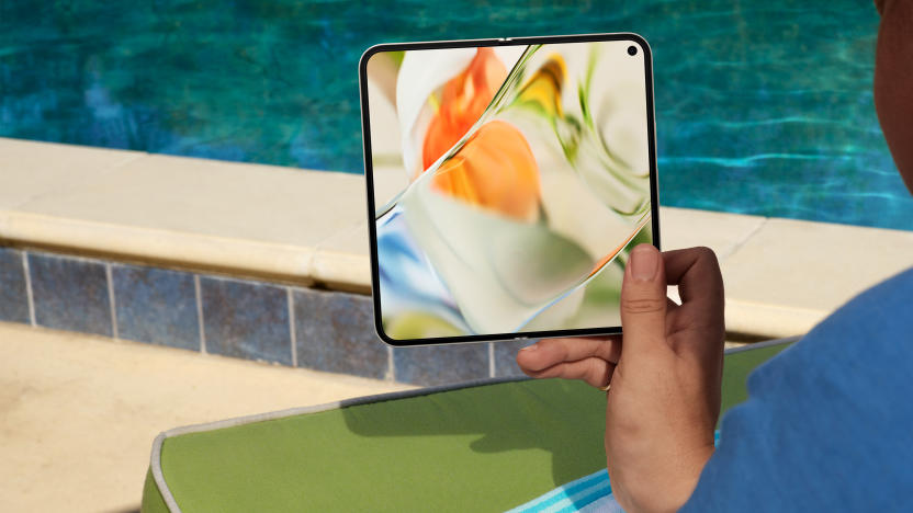 Product lifestyle image of the Google Pixel 9 Pro Fold. A person holds the (unfolded) foldable phone in their right hand while sitting poolside on a sunny day.