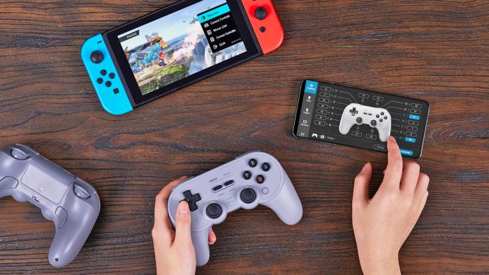 The 8BitDo wireless controller flanked by a Switch, a smartphone with controller setup graphics and two hands working the device.