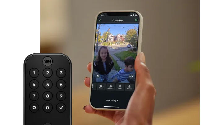 Photo of a person’s hand holding a phone running the Ecobee app. It shows a live view of two children at the door. A Yale smart lock is overlaid to the lower left.