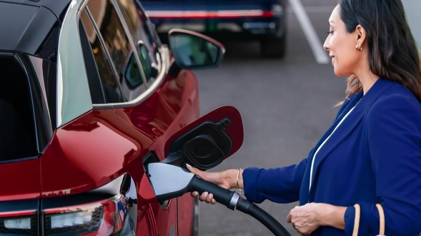 A person smiles as they place a charging cable into an electric vehicle. 