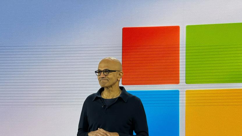 Satya Nadella on stage with the Windows logo on a screen behind him.