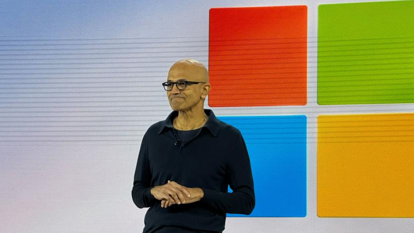 Satya Nadella on stage with the Windows logo on a screen behind him.