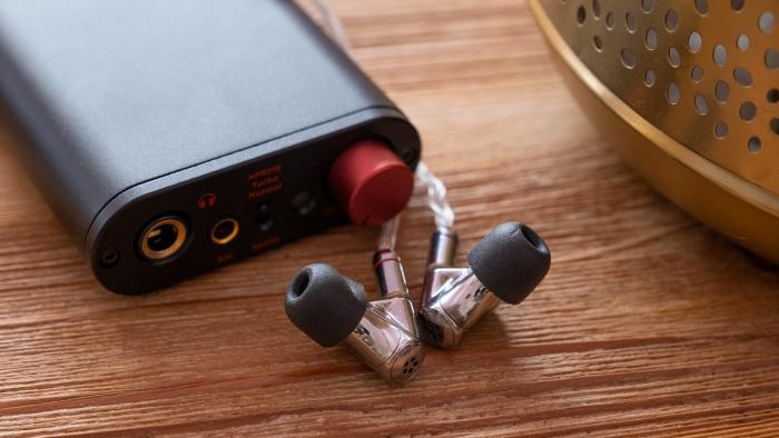 A pair of silver headphones are pictured infront of a hi-fi DAC on top of a coffee table.