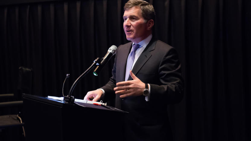 A man in a suit standing behind a podium with a mic.