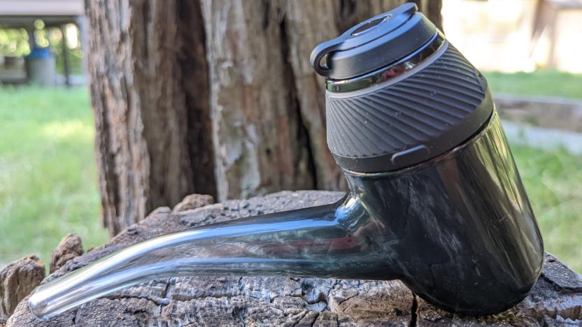 A black, pipe-shaped vape sitting on a tree stump