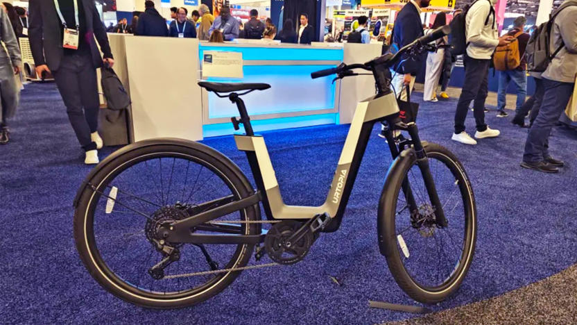 A grey, white and black Urtopia Fusion e-bike rests on its kickstand on the blue-carpeted CES 2024 showfloor.