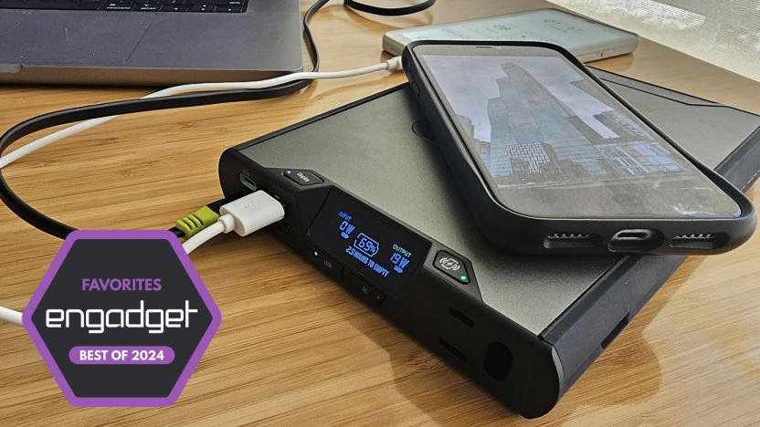 A laptop power banks sits on a desk as it simultaneously charges a phone, ereader and MacBook. 