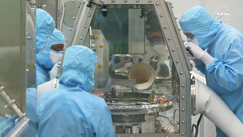 Several scientists peer into a sealed glass module where the asteroid Bennu samples stored.