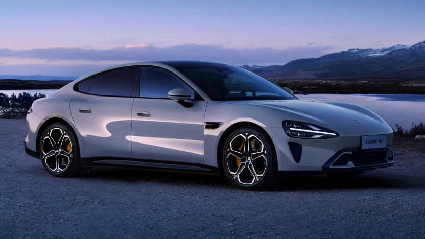 The Xiaomi SU7 electric sedan in gray is parked at dusk on a gravel road.