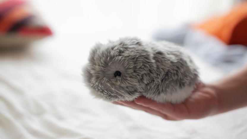 A gray plushie robot sits in a person's outstretched hand