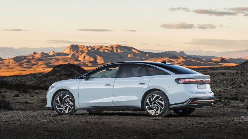 A white Volkswagen ID.7 is parked sideways at the edge of a desert and canyon landscape at dusk.