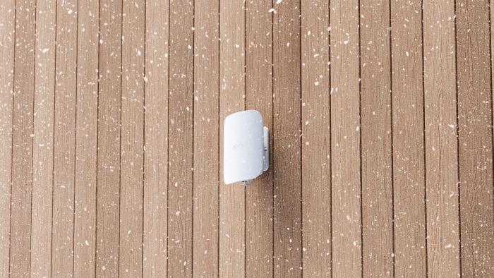 Image of the Eero Outdoor 7 on a wood wall while snow falls.