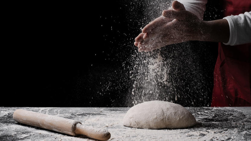 baker preparing bread dough on black table in front of yellow background